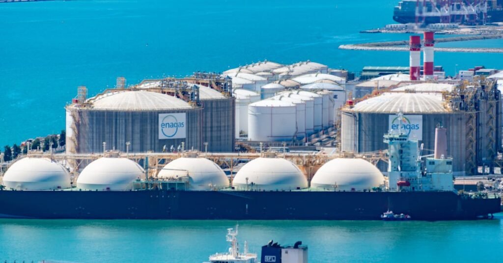 Aerial shot of a gas terminal featuring LNG storage tanks and tanker ships in turquoise waters.